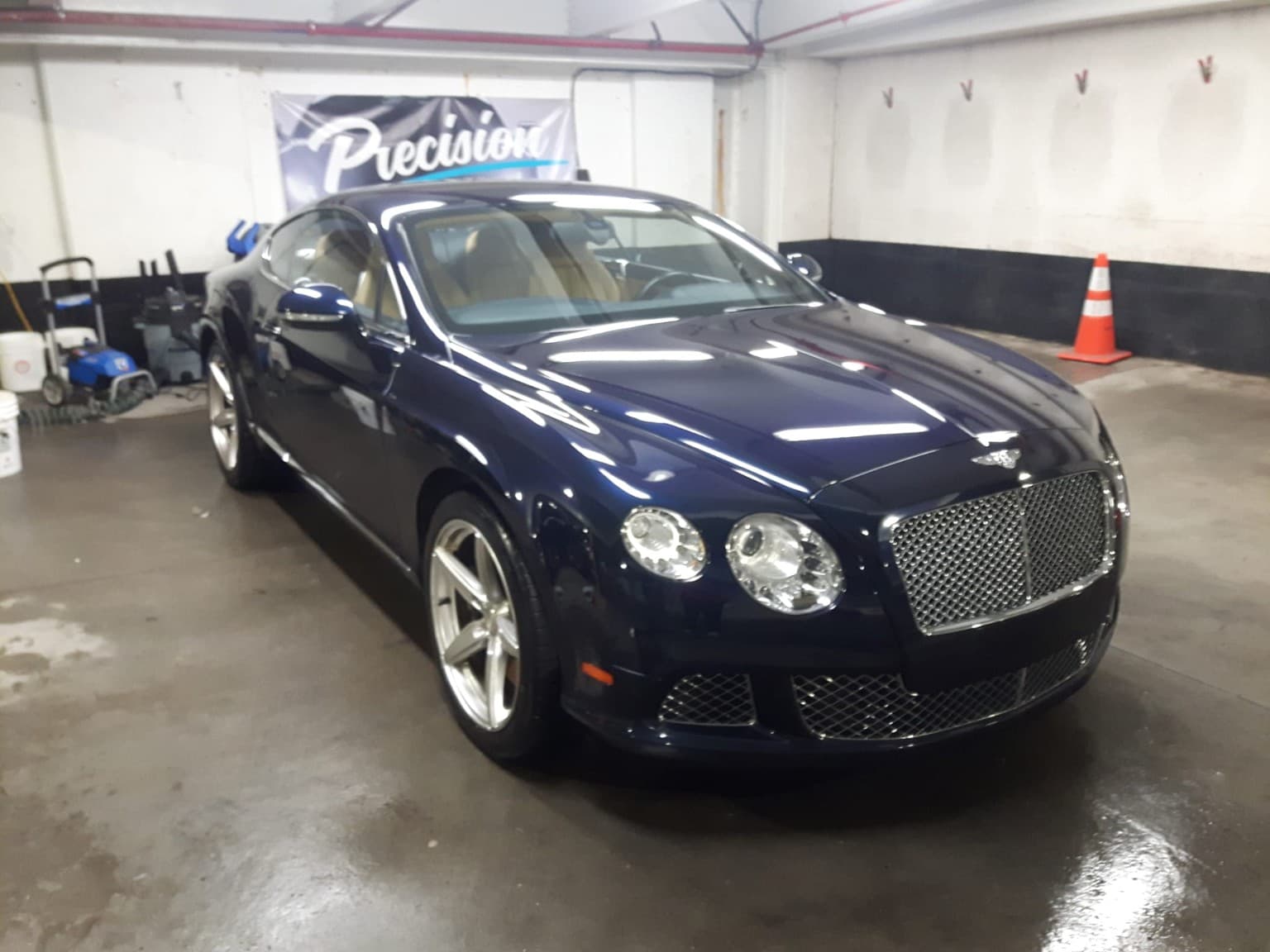 Polished navy blue Bentley Continental GT parked in a garage with detailing equipment nearby.